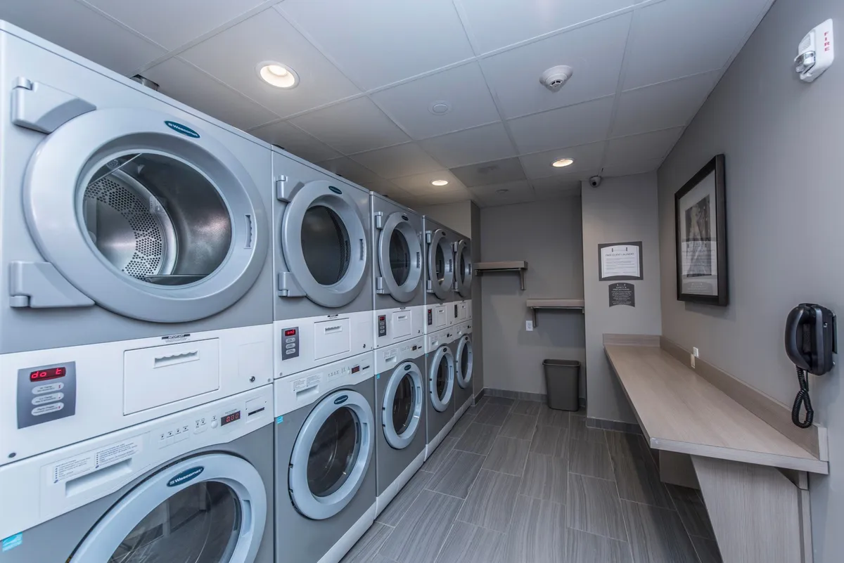 A clean, organized laundry room with rows of washing machines, a wide folding counter, and a laundry detergent dispenser. The space is practical and inviting, emphasizing convenience for guests.
