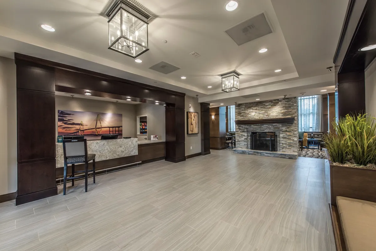 An inviting lobby with a reception desk, a warm fireplace, stylish seating, and artwork on the walls. The space radiates hospitality and comfort, perfect for first impressions or a quiet moment inside.