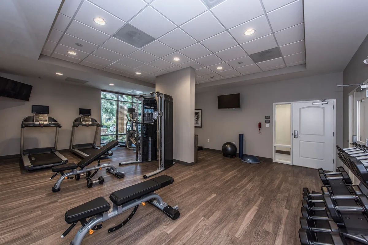 A bright, motivational fitness center equipped with treadmills, a weight machine, exercise benches, and an exercise ball. The space encourages both solo and group workouts, with ample room and modern equipment.