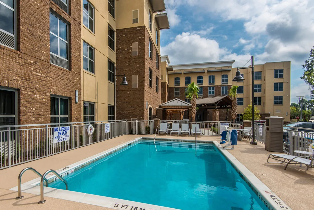 A vibrant exterior pool area with a sparkling swimming pool, lounge chairs, and an outdoor cabana. Guests are seen swimming, sunbathing, and socializing, creating a lively yet relaxed atmosphere perfect for unwinding after a busy day.